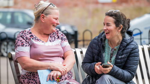 A tenant sitting on a bench speaking to a Midland Heart employee