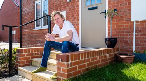 Man Sitting On The Stairs Outside Of His Home Entrance On A Sunny Day