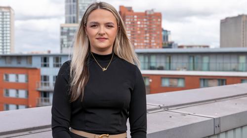 Woman Stood On A Rooftop Terrace In A Black Top With Shoulder Length Hair