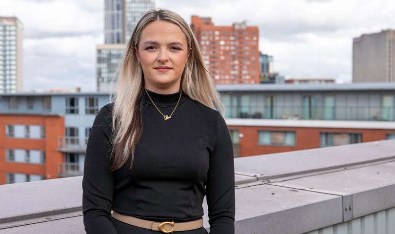 Woman Stood On A Rooftop Terrace In A Black Top With Shoulder Length Hair