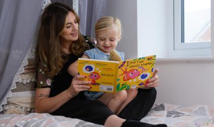 Mother And Daughter Sitting On A Bed Reading A Book Called I Don't Eat Wriggly Worms