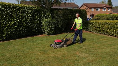 Image Of Man In High Vis Jacket With Sunglasses Operating A Lawnmower Against A Lush Green Background