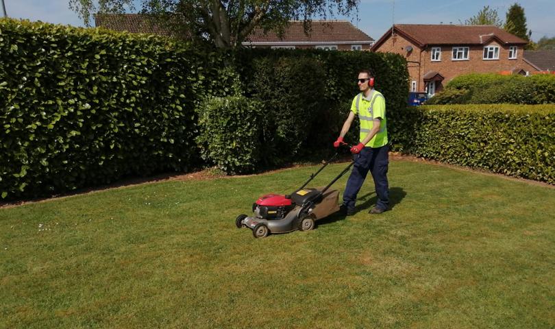 Image Of Man In High Vis Jacket With Sunglasses Operating A Lawnmower Against A Lush Green Background
